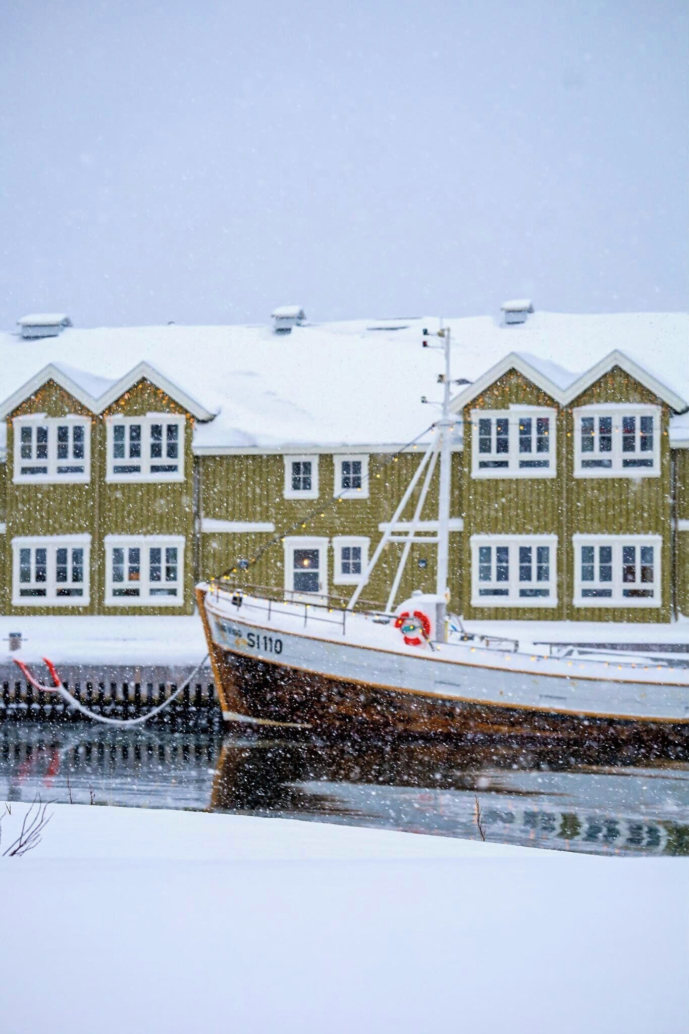 Un barco amarrado en un puerto nevado con un edificio al fondo.