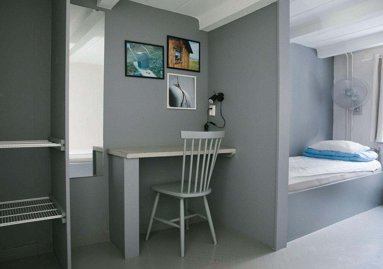 Une petite pièce comprenant un bureau, une chaise et un lit, avec une fenêtre.