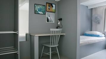 Une petite pièce comprenant un bureau, une chaise et un lit, avec une fenêtre.