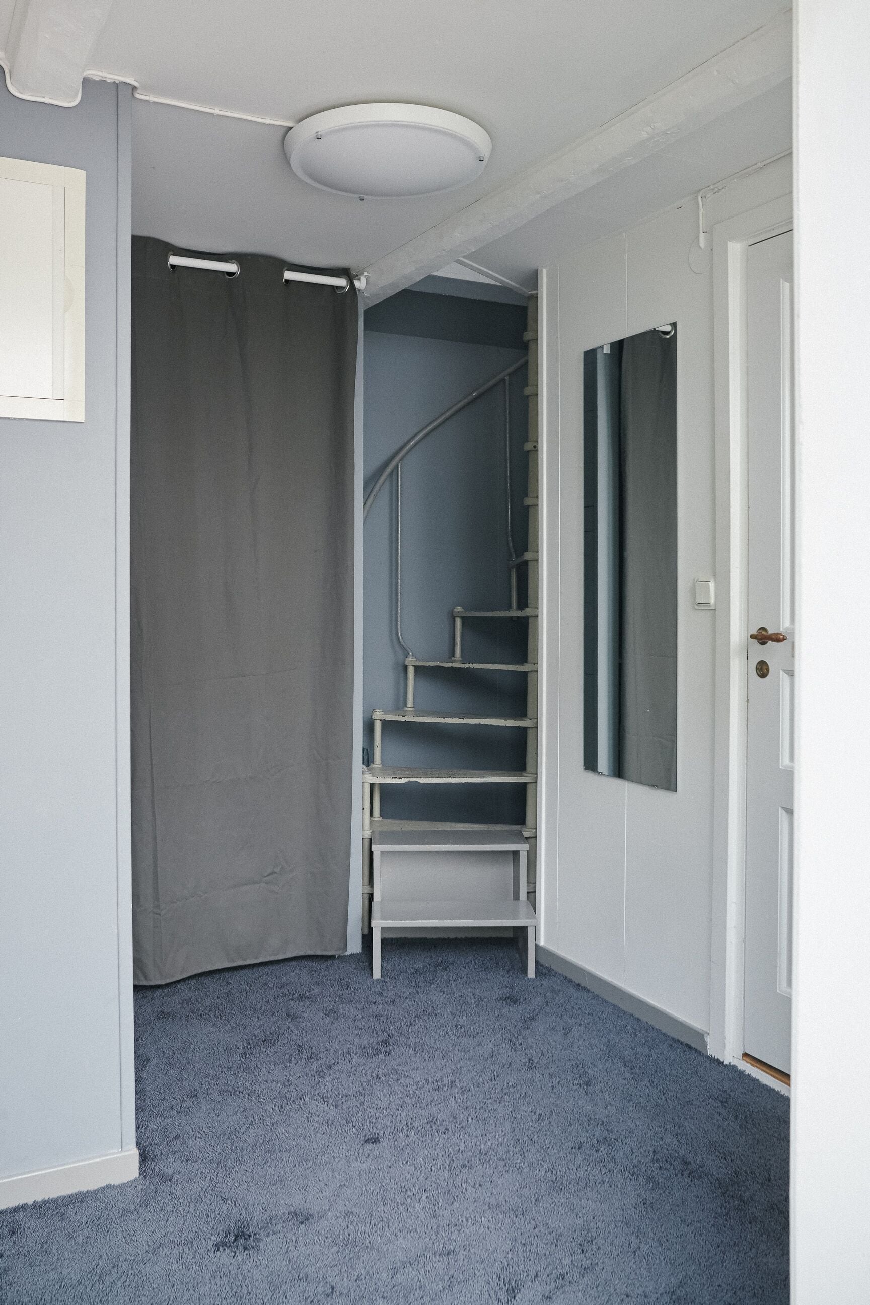 A hallway with a grey carpet, a white door, and a grey curtain.