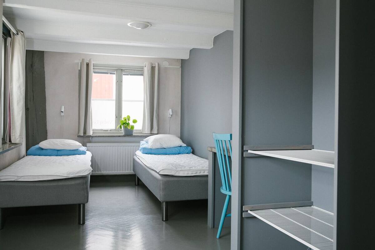 Een slaapkamer met twee bedden, een raam met gordijnen, een radiator en een plant.