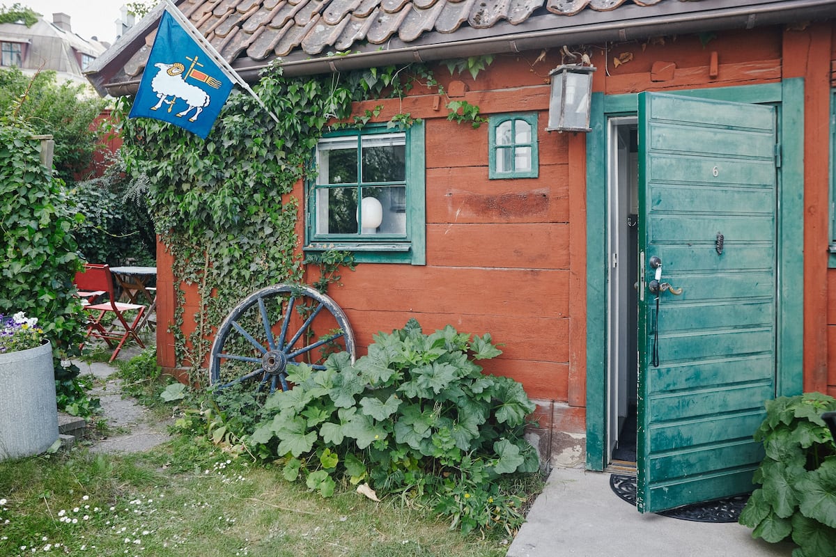 Een rustiek houten huis met een groene deur, een raam met een witte gloeilamp, en een blauwe vlag met een schapen- en vlagontwerp.