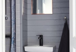 Un baño con un lavamanos blanco, un grifo negro, un espejo sobre el lavamanos y una cortina de ducha con estampado de hojas.