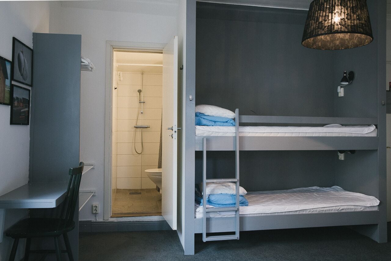 Een kleine kamer met een stapelbed, een bureau, een stoel en een douchehoek.