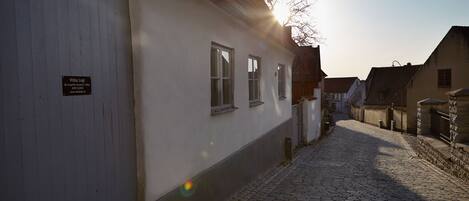 A cobblestone street with a white building featuring a signboard, a wooden door, and a window.