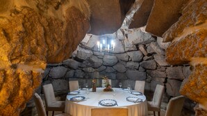 A round table set for six with a chandelier above, surrounded by stone walls and chairs. - Hotel Restaurante Asador de Roxos Casa de Albardonedo (Santiago de Compostela)
