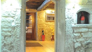 A stone-walled room with a wooden door, a tiled floor, and a small shelf with a vase. - Hotel Restaurante Asador de Roxos Casa de Albardonedo (Santiago de Compostela)