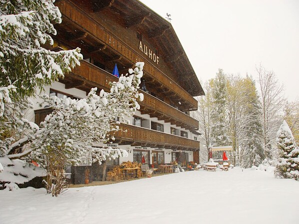 Un edificio de madera tradicional con varios balcones, rodeado de árboles cubiertos de nieve.
