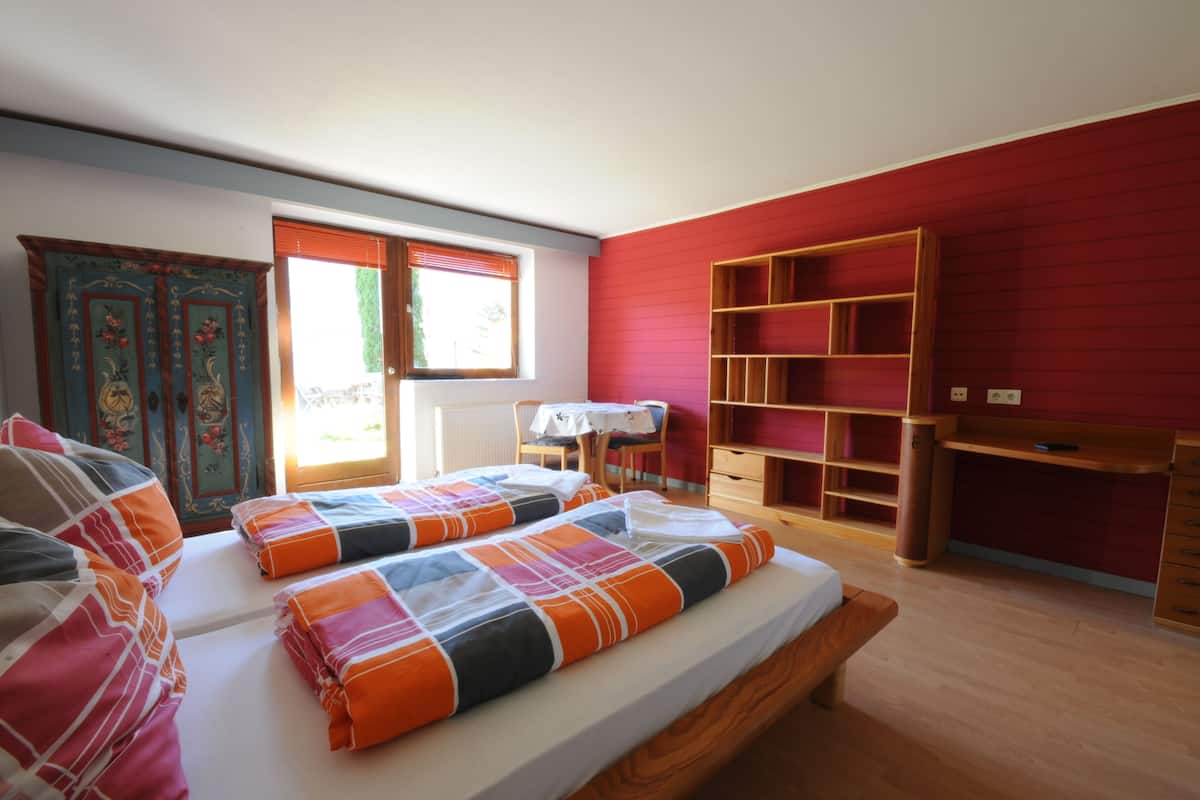 Un dormitorio con dos camas, un escritorio de madera, una silla, una estantería y una ventana con persianas.