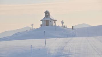 A snow-covered landscape with a small building on a hill, surrounded by snow and a clear sky.