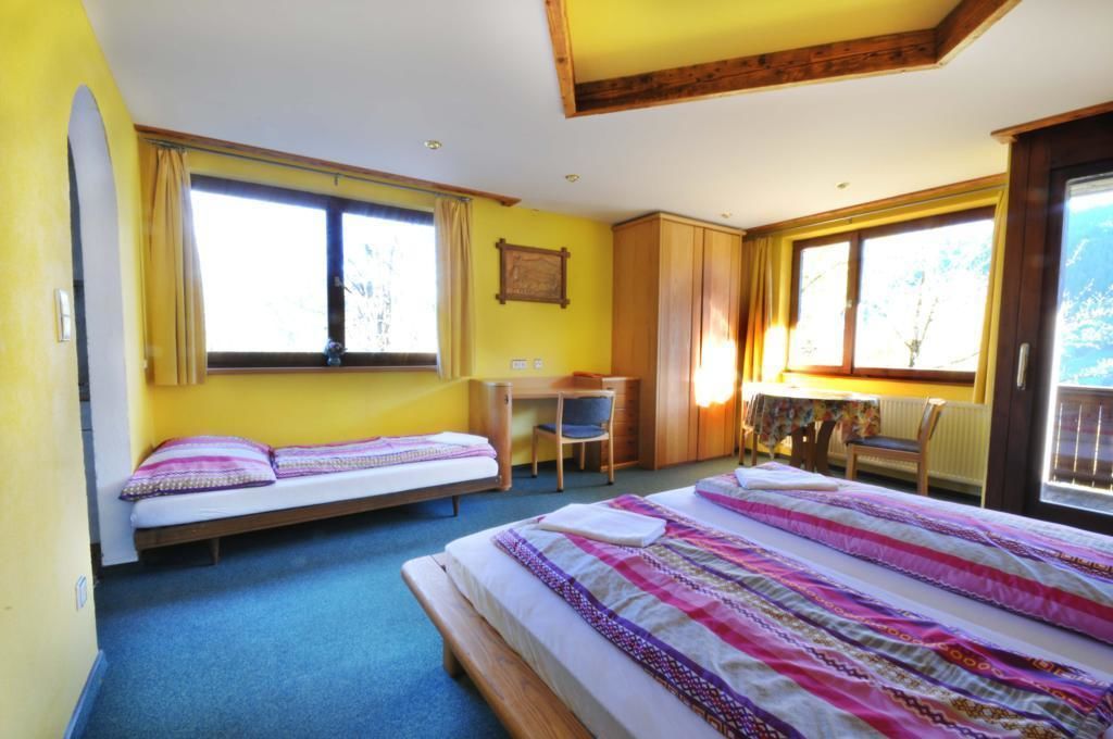 Ein Zimmer mit zwei Einzelbetten, einem Schreibtisch, einem Stuhl und einem Tisch mit Blick ins Freie.
