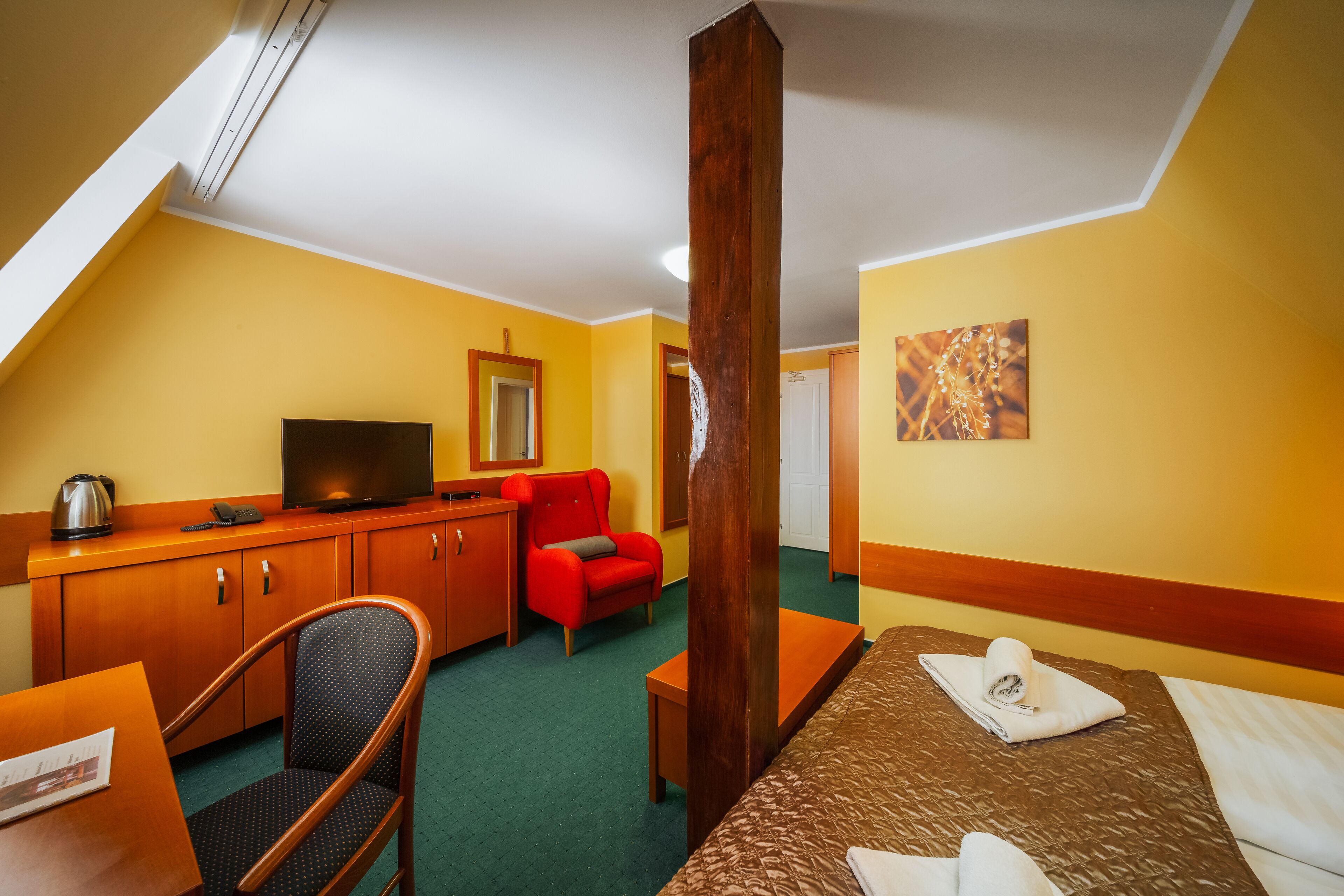 A hotel room with a bed, a desk, a chair, a television, and a red armchair.