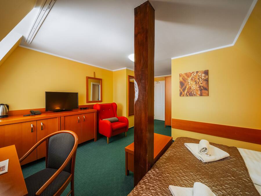 A hotel room with a bed, a desk, a chair, a television, and a red armchair.