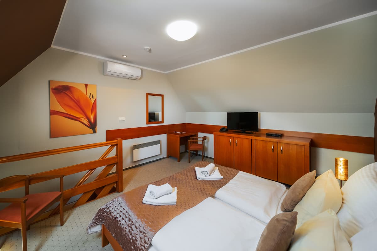 A hotel room with a bed, a desk, a chair, a TV, and an air conditioning unit.