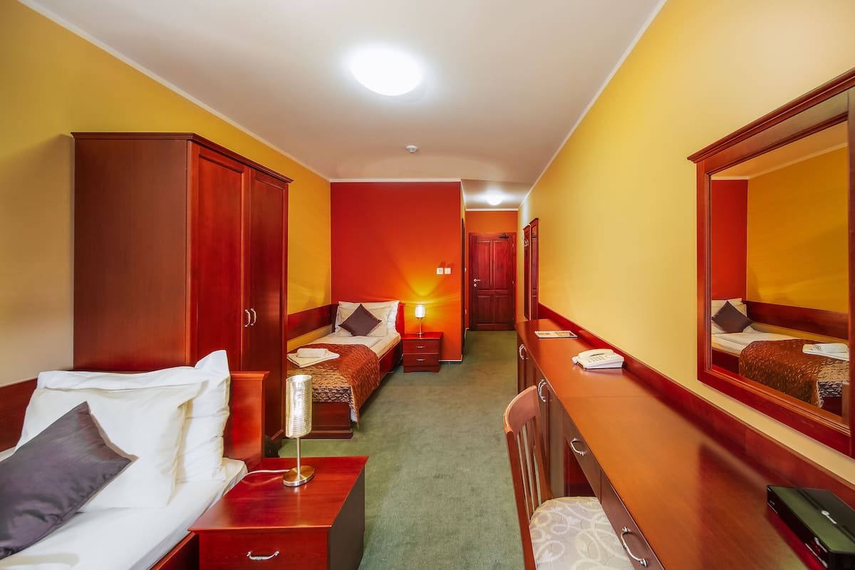 A hotel room with a bed, a desk, a dresser, a mirror, and a door leading to another room.