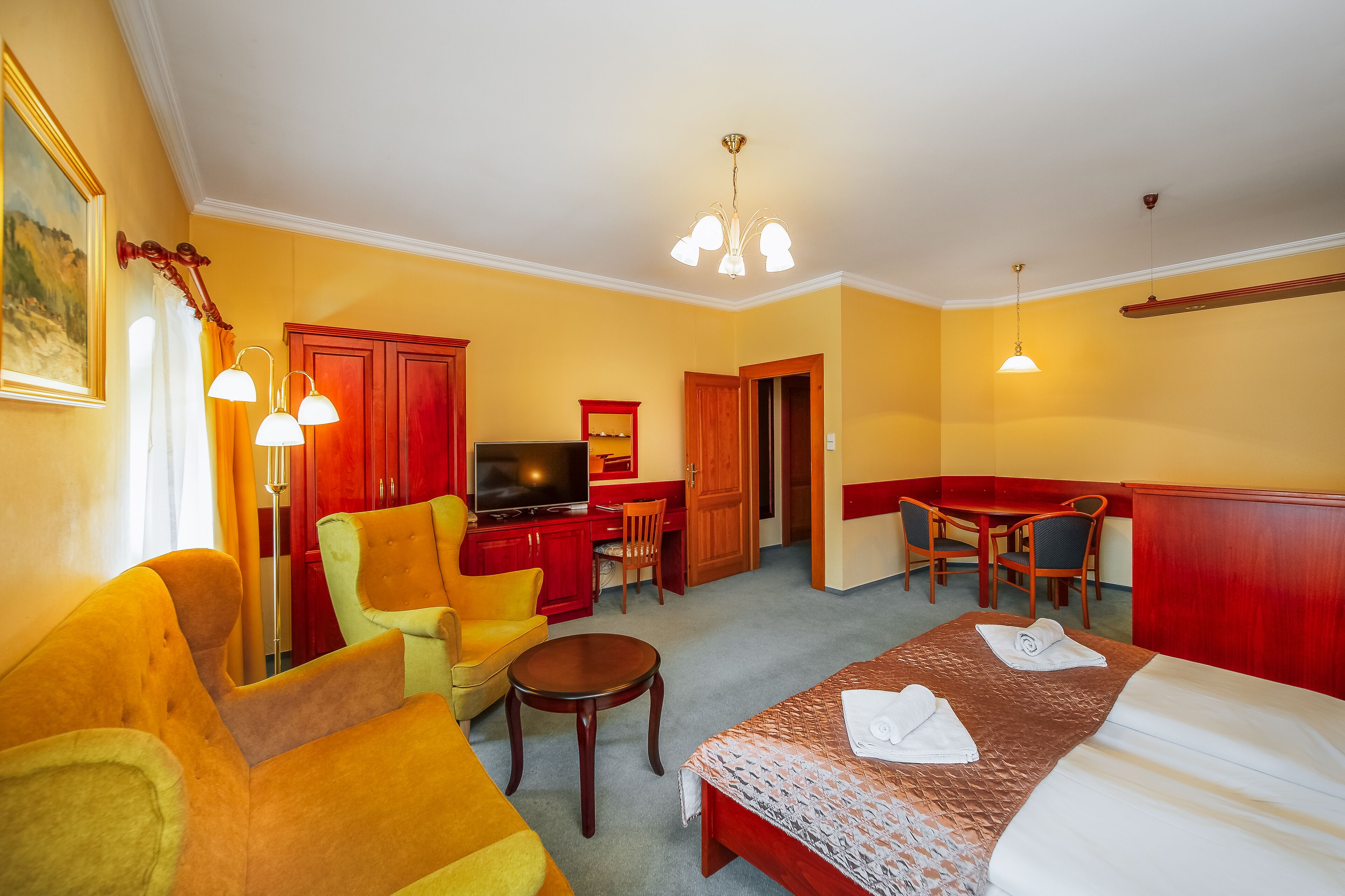 Quarto de hotel com uma cama, televisão, escrivaninha e duas cadeiras.