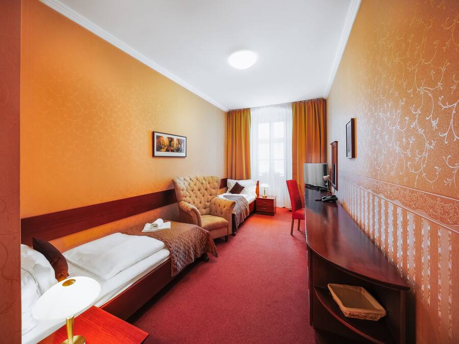 A hotel room with two single beds, a sofa, a TV, and a desk.