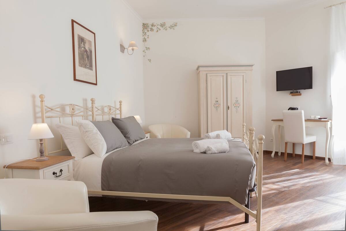A neatly arranged bedroom with a bed, bedside table, chair, desk, and TV.