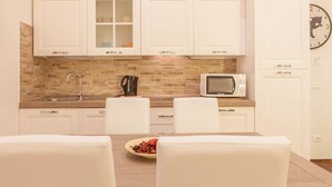 Una cocina moderna con armarios blancos, protector contra salpicaduras de piedra, un microondas y un reloj en la pared.