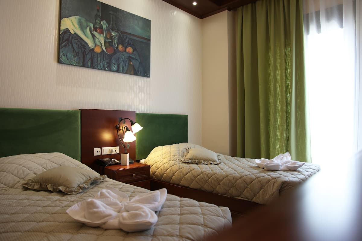 Ein Hotelzimmer mit zwei Betten, einem Bild an der Wand und einem grünen Vorhang.