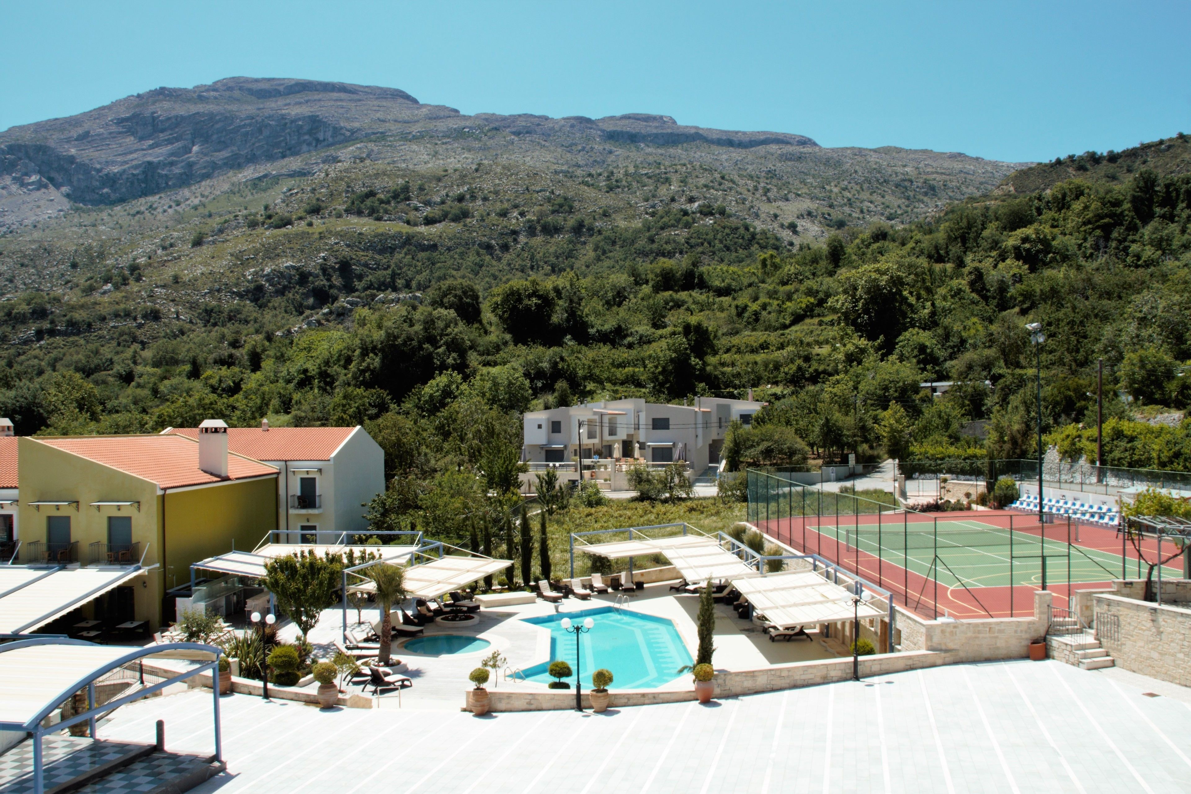 A hotel with a pool, tennis court, and mountainous backdrop.