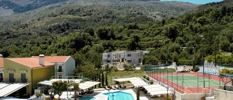 A hotel with a pool, tennis court, and mountainous backdrop.