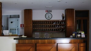 A reception desk with a clock, a sign prohibiting smoking, and a display of brochures and a plant. - Hotel San Giuseppe (Pozzuoli)