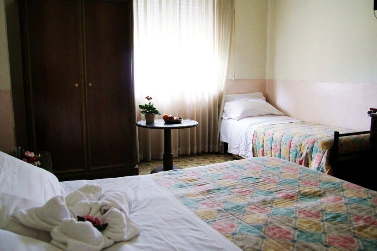 A hotel room with two beds, a small table with a plant, and a wardrobe.
