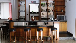 A bar area with wooden stools, a countertop with bottles, glasses, and a microwave. - Hotel San Giuseppe (Pozzuoli)