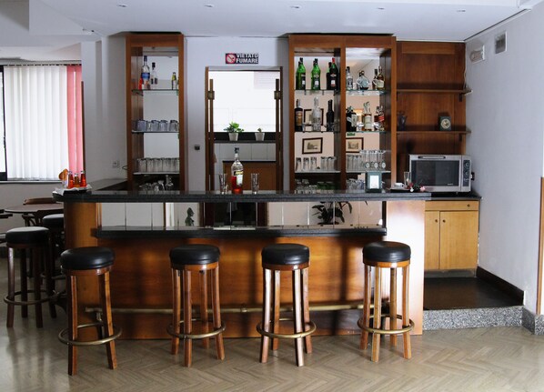 A bar area with wooden stools, a countertop with bottles, glasses, and a microwave. - Hotel San Giuseppe (Pozzuoli)