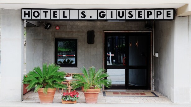 The entrance of Hotel S. Giuseppe with a sign above the door, potted plants in front, and a window with a view of greenery. - Hotel San Giuseppe (Pozzuoli)