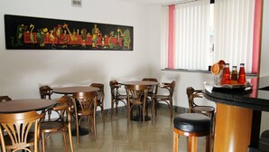 A dining area with multiple wooden tables and chairs, a large mural on the wall, and a window with blinds. - Hotel San Giuseppe (Pozzuoli)
