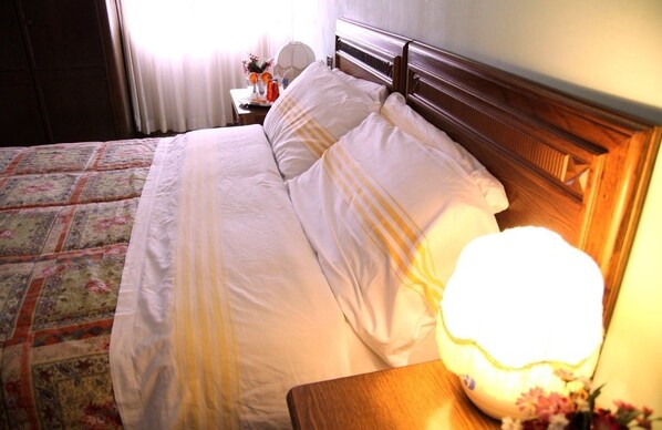 A neatly made bed with white linens and a striped pillow, a bedside lamp, and a floral arrangement on a nightstand.
