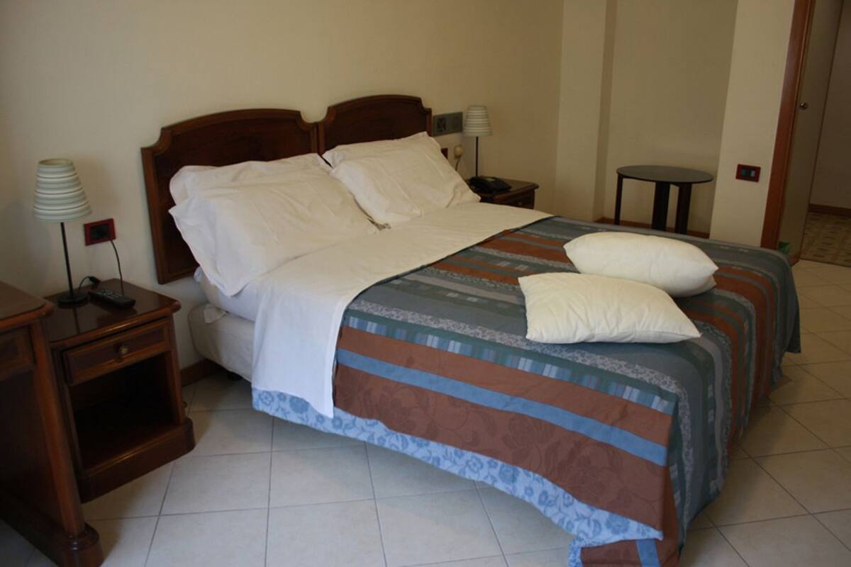 A hotel room with a double bed, two bedside tables, a lamp, and a small table.