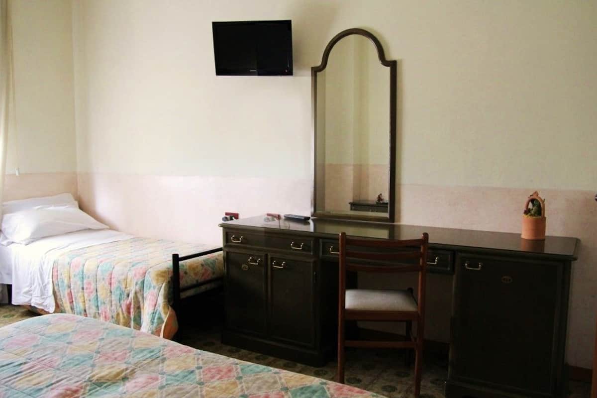 A bedroom with two beds, a dresser, a chair, a mirror, and a television on the wall.