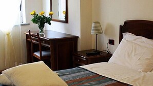 A hotel room with a bed, a bedside table with a lamp, a dresser, and a vase with flowers. - Hotel San Giuseppe (Pozzuoli)
