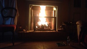 Una habitación con chimenea, una silla y una mesa con una botella.