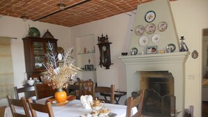 Un comedor con una mesa dispuesta para una comida, rodeada de sillas de madera. Se observa una chimenea con repisa al fondo.