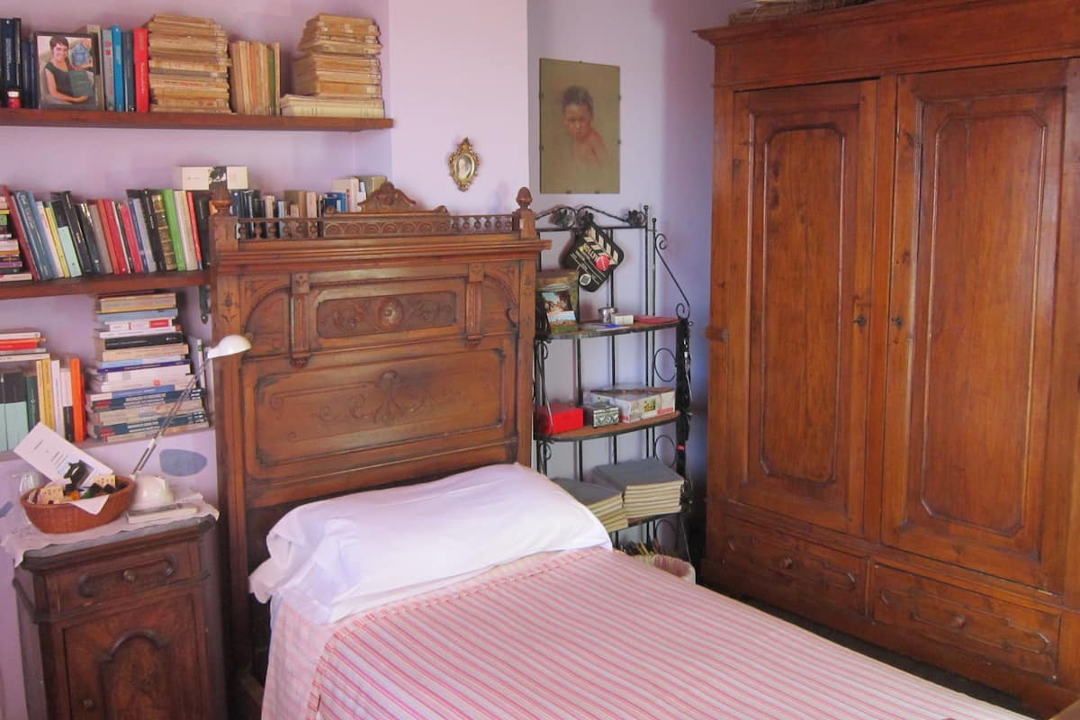 Une chambre à coucher avec un lit en bois, une table de chevet, une bibliothèque remplie de livres et une armoire.