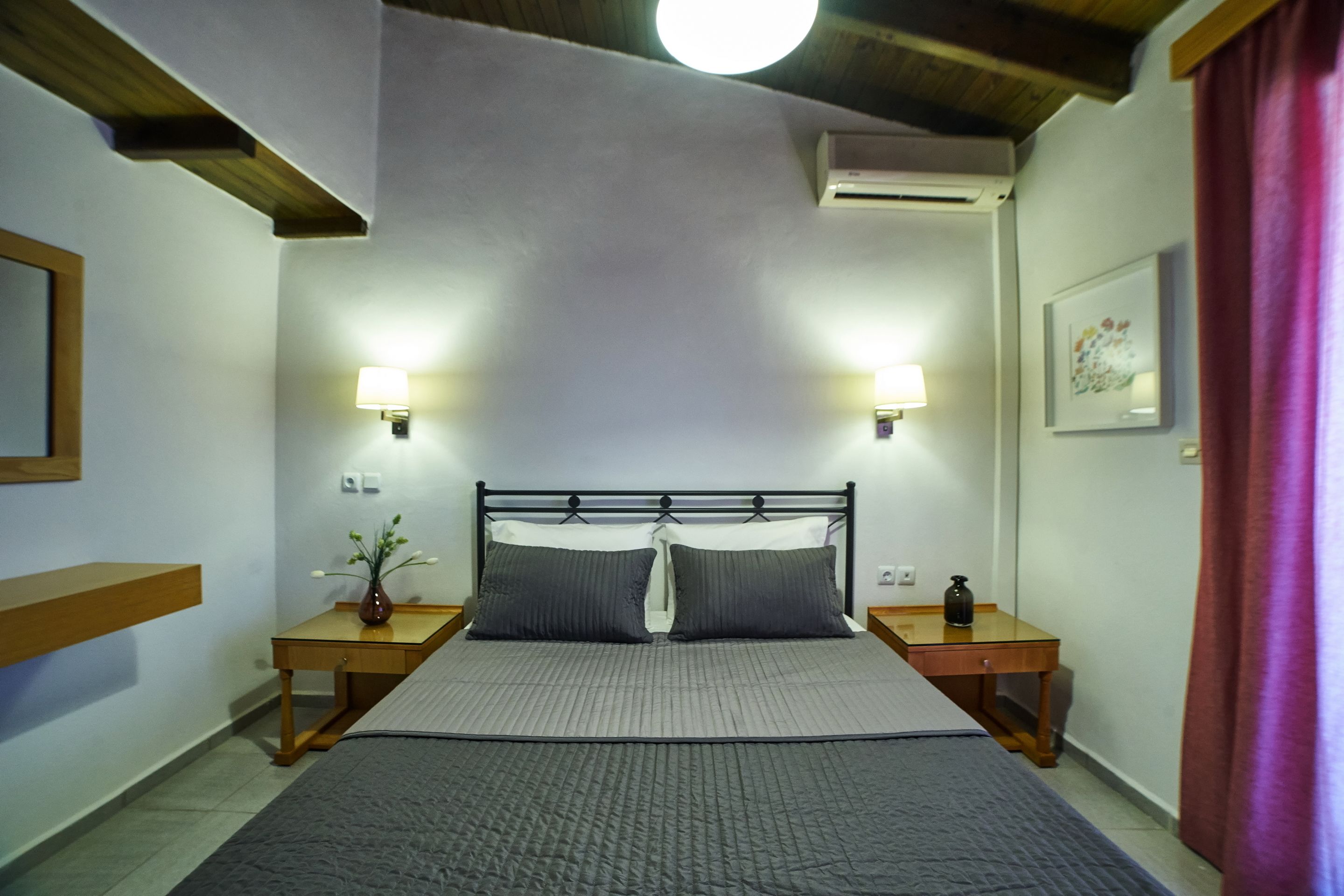 Ein Schlafzimmer mit einem großen Bett, zwei Nachttischen, einem Beistelltisch, einer Wand-Klimaanlage und einer Deckenleuchte.