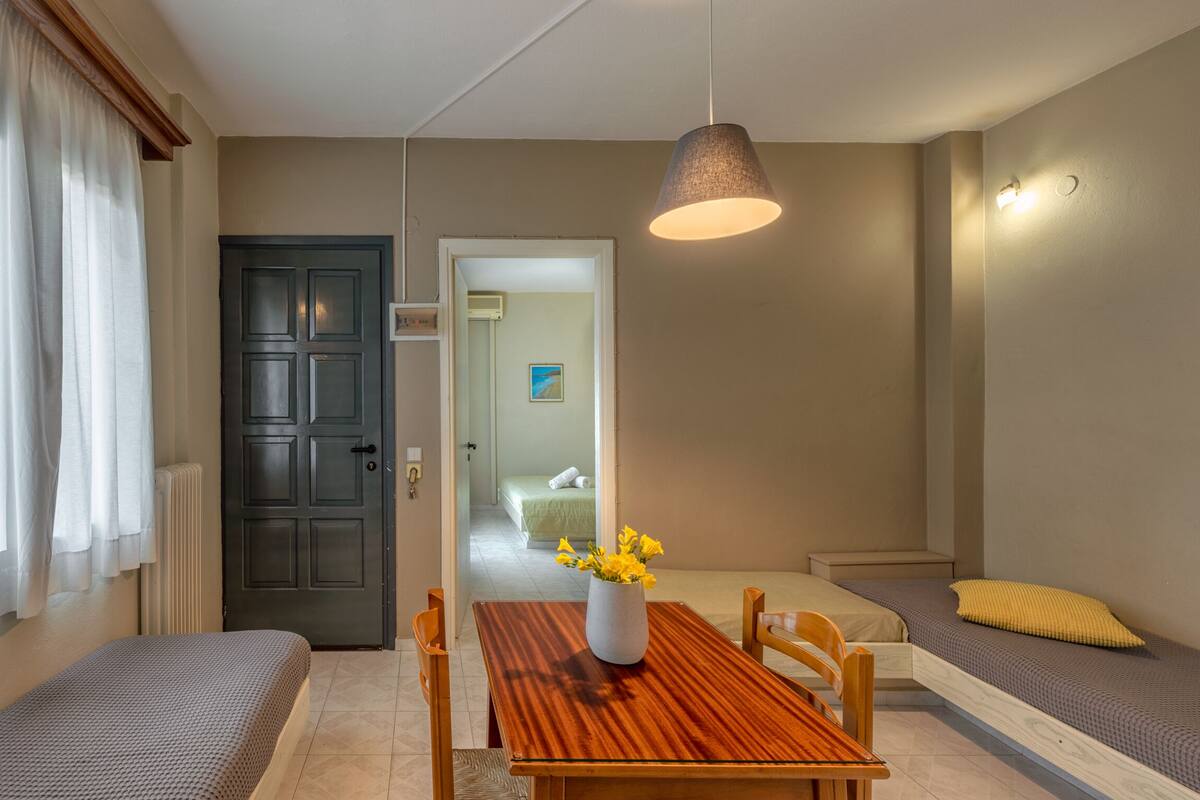 Een kleine kamer met een houten eettafel, een bank, een bed en een deur naar een andere kamer.