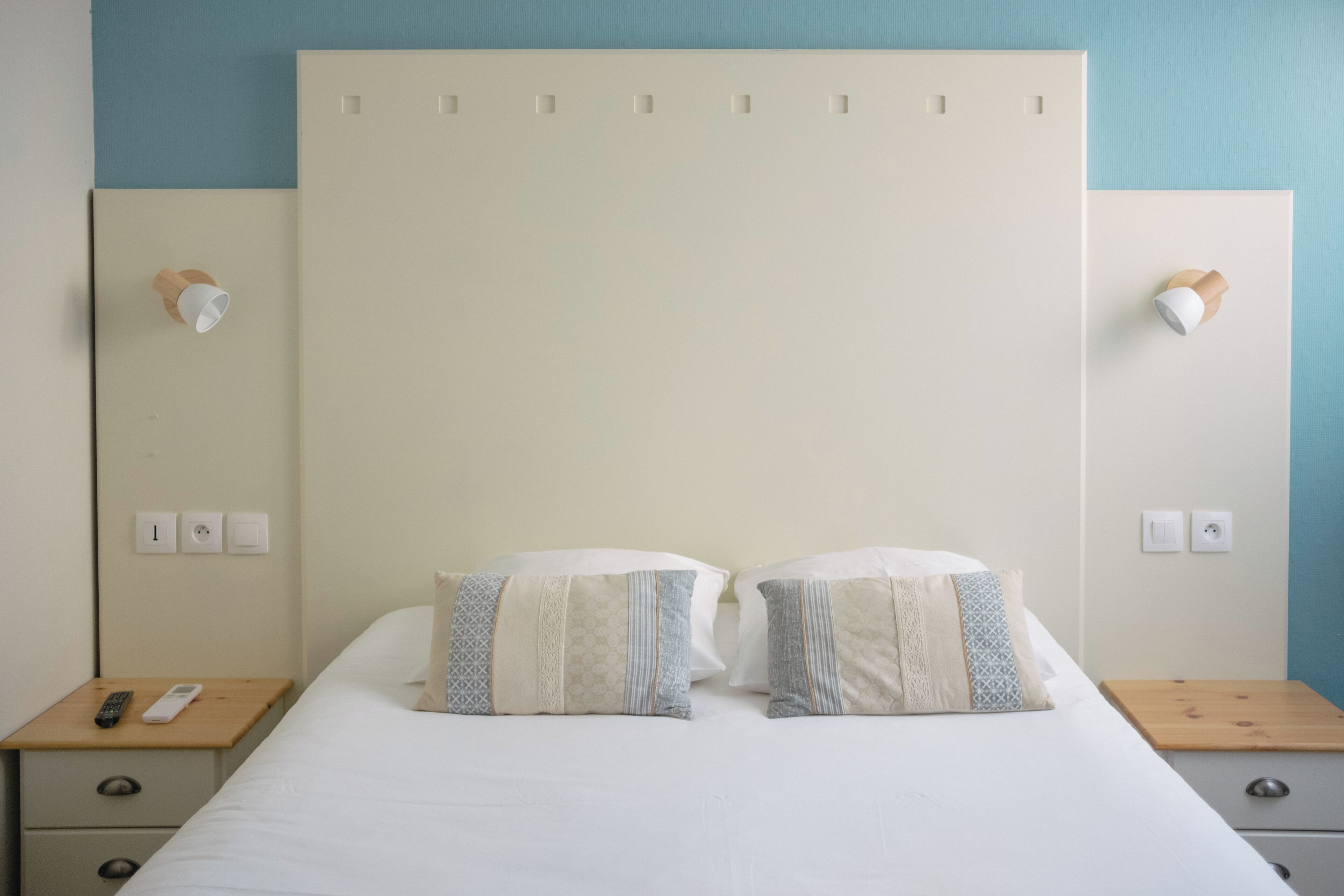 A neatly made double bed with two pillows, bedside tables with lamps, and a wall-mounted light fixture.