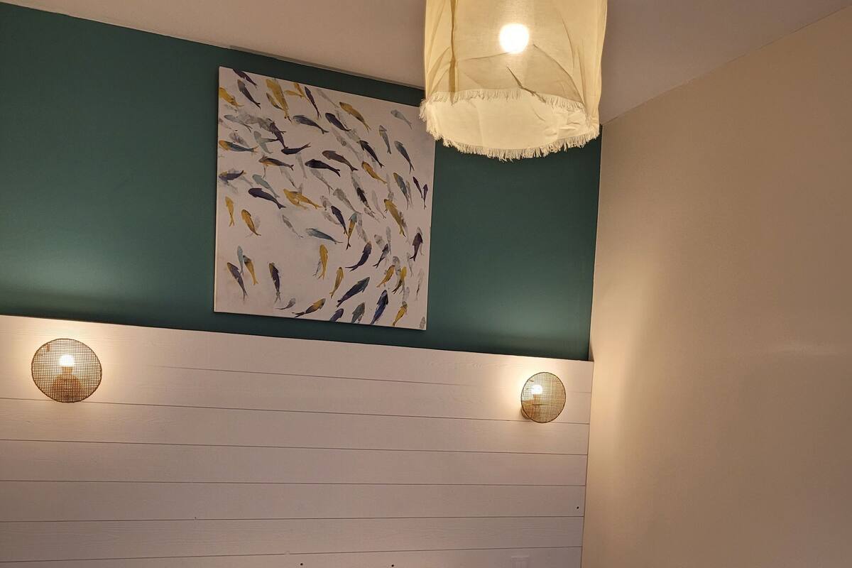 A bedroom with a bed, two wall-mounted lights, a wall art of fish, and a ceiling light fixture.