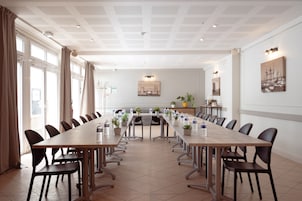 Uma sala de conferência com uma mesa comprida, cadeiras, plantas em vasos e um quadro na parede.