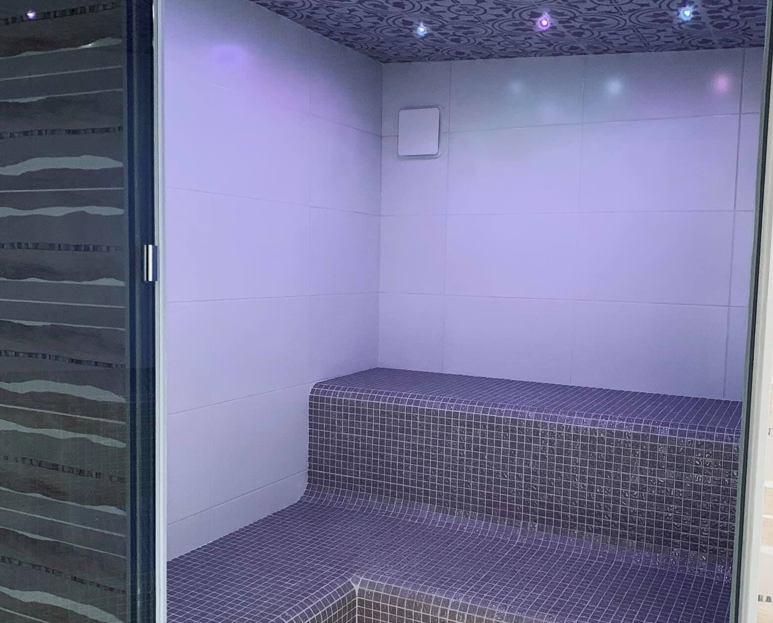A small, enclosed space with tiled walls and a patterned ceiling, featuring a single light fixture and a ventilation unit.