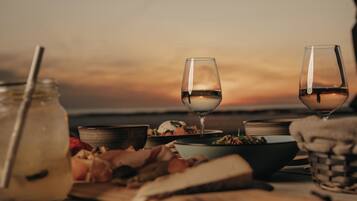 A table set with wine glasses, a jar, bowls, and a basket, with a sunset in the background.