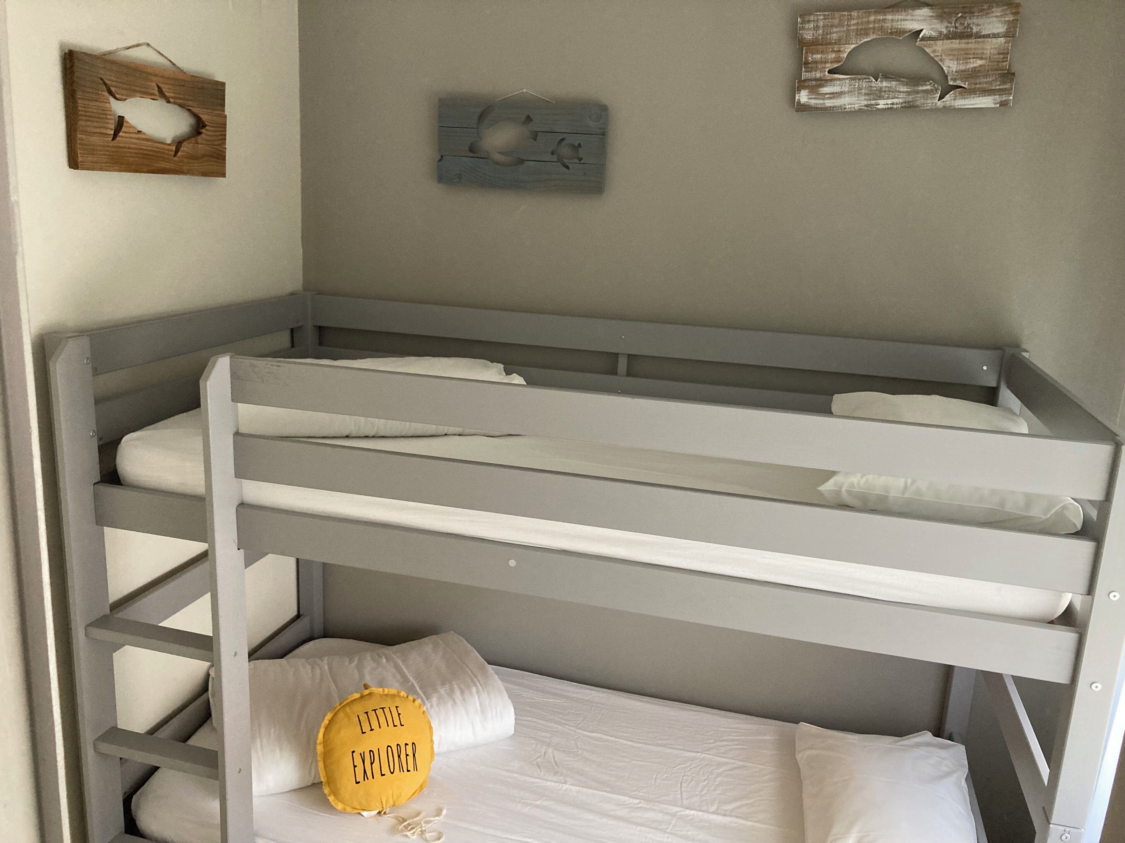Een stapelbed met witte beddengoed en een geel kussen met de tekst 'LITTLE EXPLORER'.