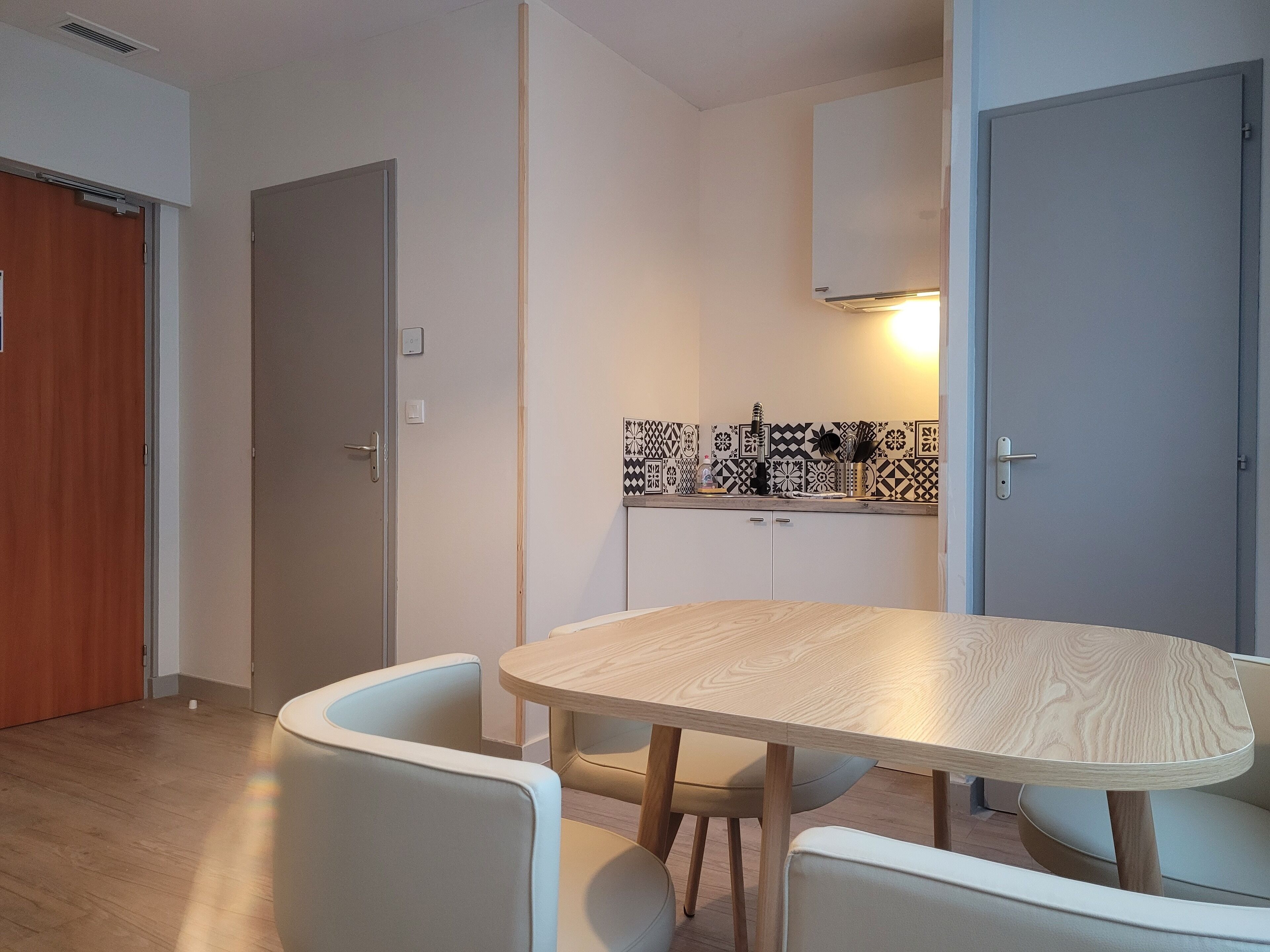 A modern kitchen with patterned backsplash tiles, a round wooden table with chairs, and a built-in oven.