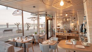 A cafe with tables and chairs, a counter with kitchen items, and a view of the sea. - Hôtel Le Rivage (Chatelaillon-Plage)