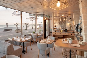 Um café com mesas e cadeiras, um balcão com utensílios de cozinha e vista para o mar.